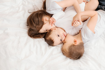Three young children lie in bed and cuddle, view from above. siblings, large family