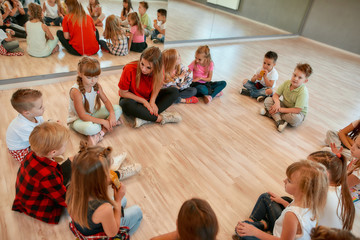 Analyzing mistakes. A group of little dancers sitting on the floor gathered around their female dance teacher and listening her carefully. Dance school