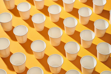 White paper cups of coffee on yellow paper light background.