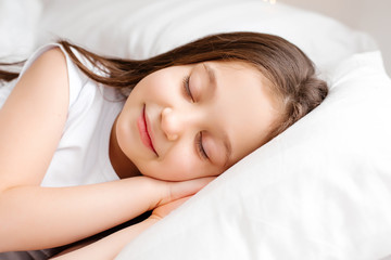 Obraz na płótnie Canvas Little brunette girl sleeps sweetly in bed with white linen. space for text. healthy baby's sleep