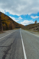 Road in the autumn mountains. Altai, Siberia, Russia. Yellow autumn forest and mountains with clouds.