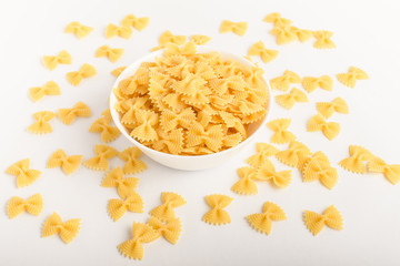 Dried Farfalle Rigate traditional Italian pasta on a plate ready to be cooked, isolated on a white table, side viewof healthy food 
