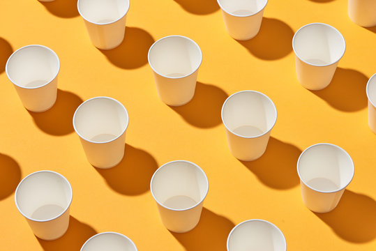 White paper cups of coffee on yellow paper light background.