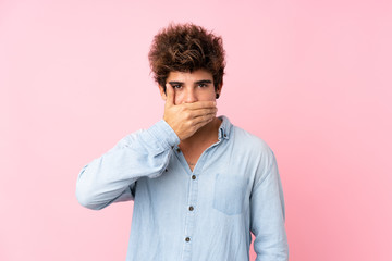 Young caucasian man with jean shirt over isolated pink background covering mouth with hands