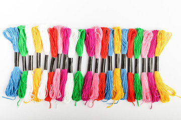 Many mixed vivid colored sewing threads for embroidery displayed in a circle isolated on a white table, top view or flat lay of red, pink, yellow, blue, black and green textile materials

