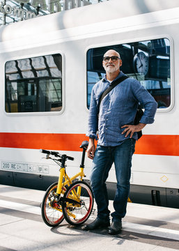 Older Man Waiting in Front of Train With Folding Bike