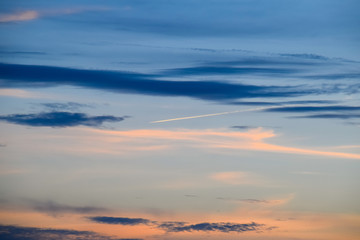 Contrail from airplane on a blue sky against a sunset.