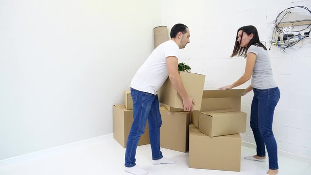 Tired guy is bringing heavy boxes in room suffering from backache touching back with unhappy face during relocation.