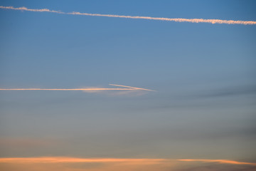 Contrail from airplane on a blue sky against a sunset.