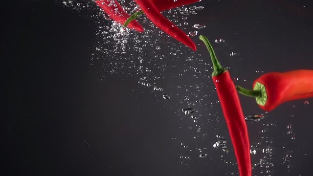 Hot red chilli peppers falling into the water on a black background. Slow motion