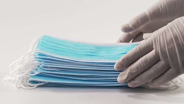 Nurses' hands remove a stack of medical masks from a white sterile surface. Medical mask closeup on a white background.