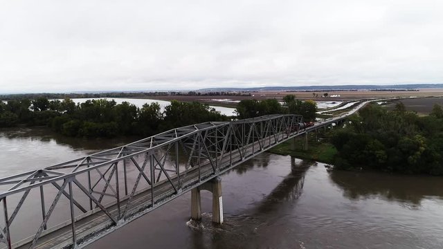 Cars drive over river bridge on overcast day, aerial