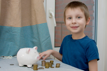 A beautiful, sweet boy, a preschooler counting his savings. The coins are stacked. There is a piggy...