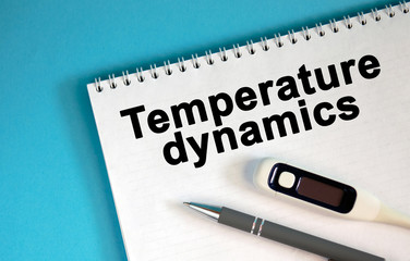 Obraz premium TEMPERATURE DYNAMICS - text on a notepad. Lie a pen and a medical thermometer