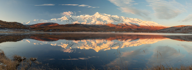 Wonderful sunrise landscape panorama of Kurai steppe with chuya river, mountain ice peaks of Siberia and sunny sky of Altai background. Natural scenery of autumn mountain forest. Altai, Siberia.