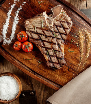 grilled t-bone steak served with salt herbs and grilled cherry tomatoes