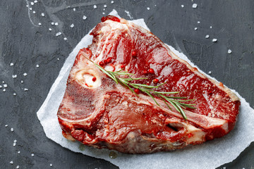 Raw fresh meat t-bone steak with spices on a dark background, close up