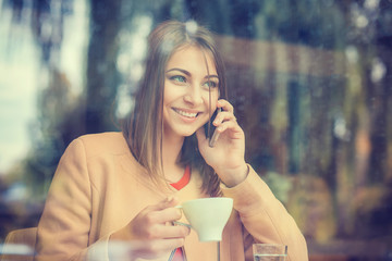 Businesswoman drinking coffee / tea and using phone computer in a coffee shop