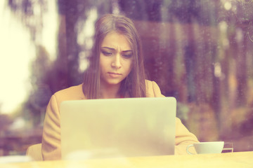 woman upset sitting in cafe in front of laptop holding screen in hands