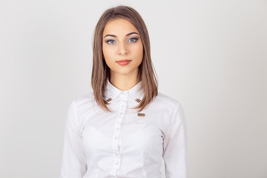 Portrait serious young business woman wearing white shirt, looking to you camera, isolated white background. One single person. Neutral human emotion facial expression feeling.