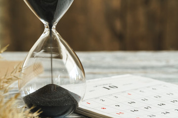 Hourglass with calendar on wooden desk close up. Time concept