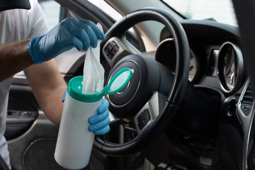 A bearded brown haired man wearing a baseball cap uses alcohol wipes to sterilize the front driver...