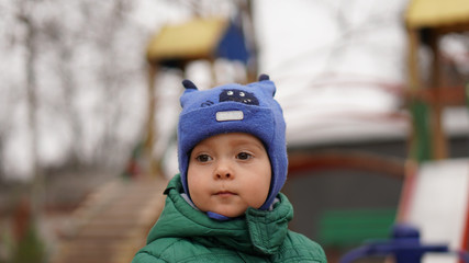 Portrait of little cute boy in a green jacket and hat with horns in the park