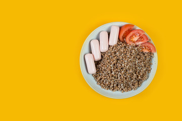 A plate of cooked buckwheat, sausage and tomato on a yellow trend background