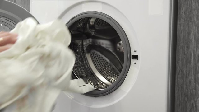 Female hand with married ring takes WHITE CLOTHES from laundry machine. Loading washing machine. Load clothes to washer machine. Load clothes laundry washing machine. Preparing laundry washing