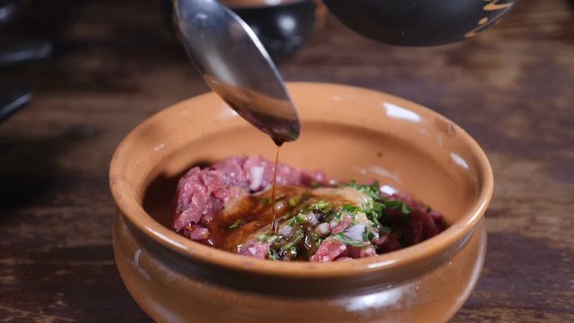 Close-up shot of male chef in black gloves preparing gourmet dish of meat tartare and mixing salad ingredientsin bowl. Kitchen in restaurant, food video, slow motion. Full hd