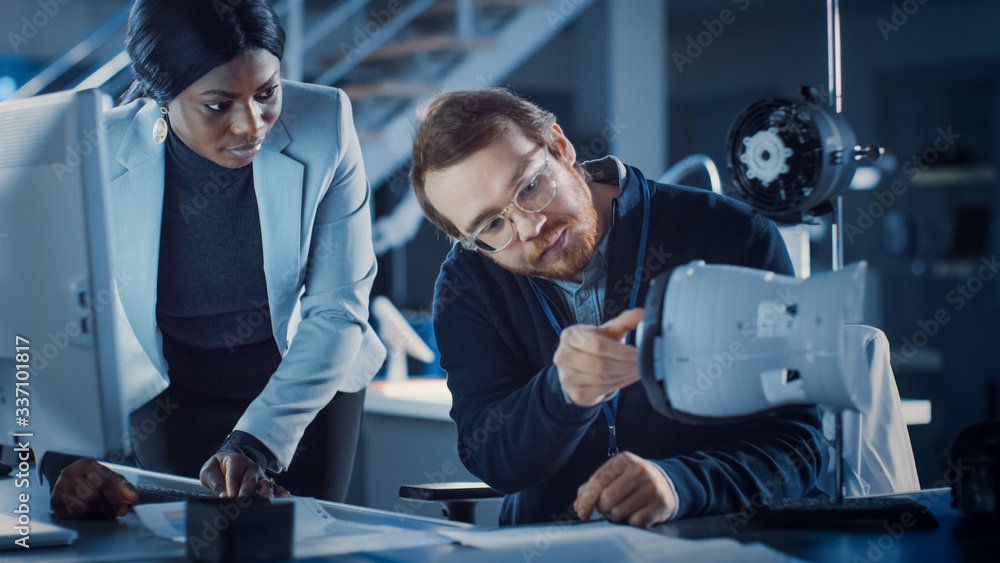 Poster Electronics Development Engineer Working at His Desk, Talks with Project Manager, Shows High Tech Prototype Component. Team of Professionals Working in the Modern Technology Designing Agency. 