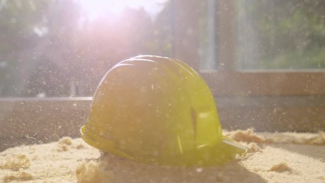 SLOW MOTION, LENS FLARE, CLOSE UP, DOF: Bright sunbeams shine on yellow hard hat crashing on a dusty panel polyurethane foam. Clumsy contractor drops his hard hat on a dusty piece of insulation foam.