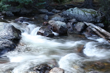 Naklejka na ściany i meble Rocky Mountain waterfalls and streams with smooth flowing water over boulders in pine trees