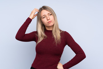 Young blonde woman over isolated blue background having doubts while scratching head