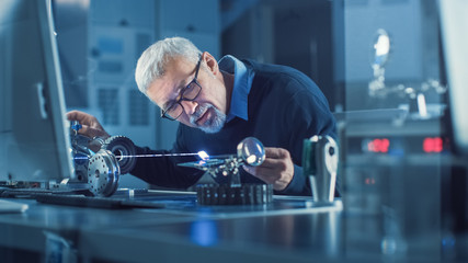 Portrait of Focused Middle Aged Engineer in Glasses Working with High Precision Laser Equipment,...