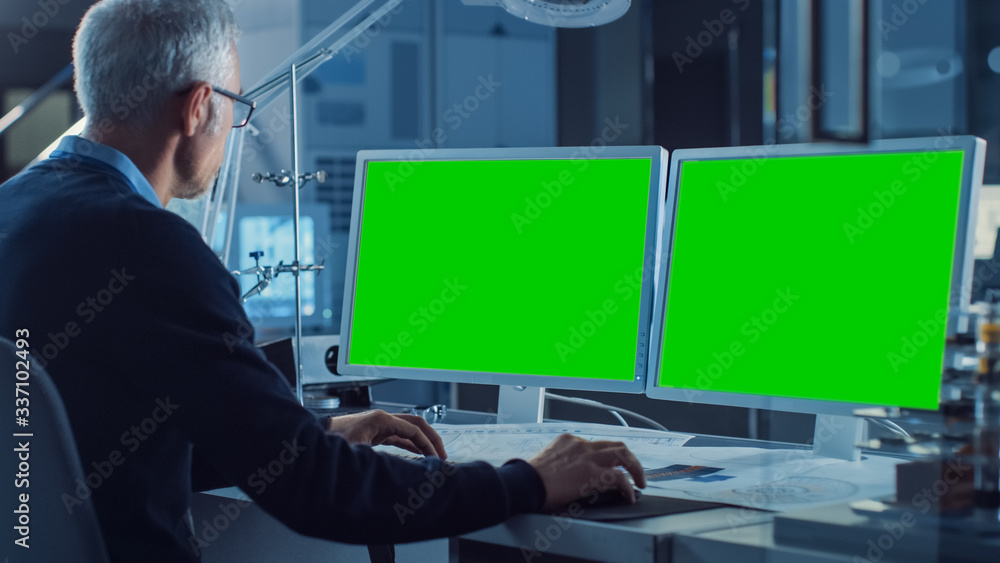 Aufkleber Professional Engineer Works on Computer with Two Green Mock-up Screen Displays. In the Background Industrial Electronics Design Agency. Over the Shoulder Shot