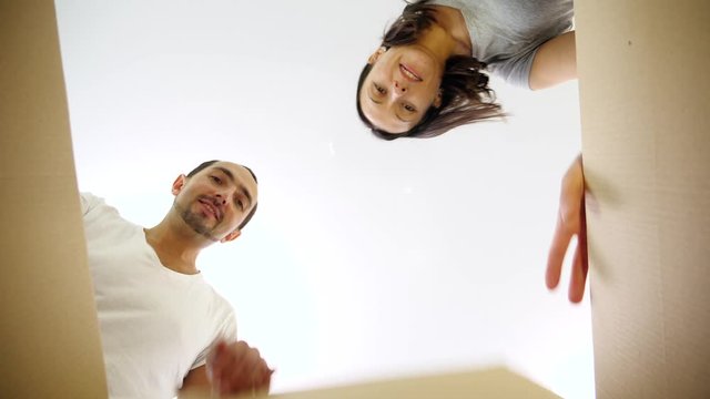 Happy couple opening a parcel box and looking inside with different emotions, being surprised.