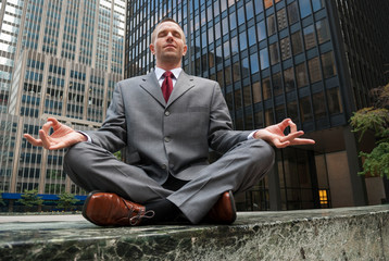 Calm businessman sitting outdoors meditating on an empty city sidewalk 