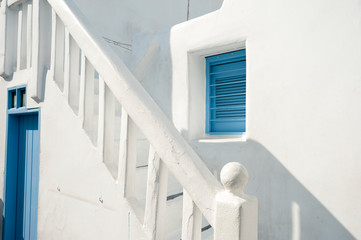 Classic Mediterranean white stucco staircase leading past matching blue window and door in a sunny alley in Mykonos, Greece