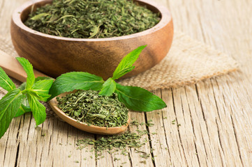 Fresh green peppermint leaves and dried mint leaves in wooden spoon on rustic table. Dry spice...