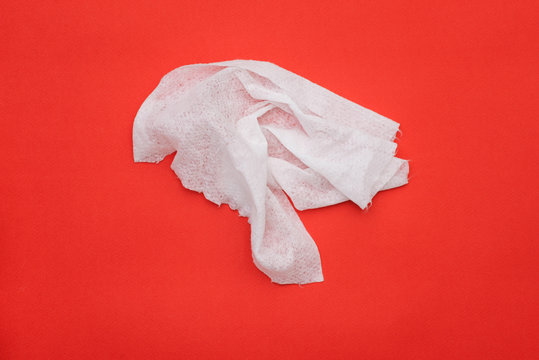 Used wet wipe on a red background. Crumpled disinfectant wipe. Disinfection against germs, viruses and infections.