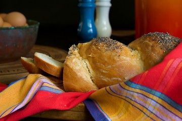 White bread load with two slices on a red and yellow striped cloth.  A bowl of eggs and a blue and...