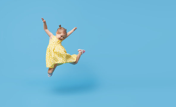 Portrait of smiling cute little toddler girl. child jumping isolated over blue background. Looking at camera and laughs