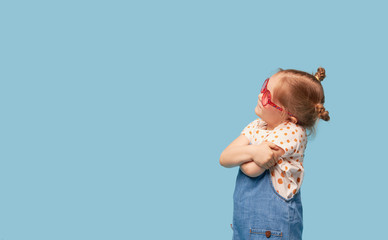 Portrait of surprised cute little toddler girl child standing isolated over blue background. Holding a gift box. Empty space for text