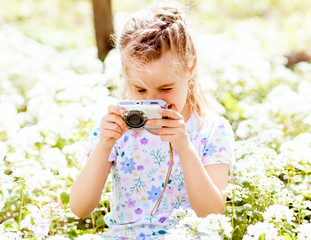 Beautiful little girl in a white T-shirt makes a photo of yellow flowers using a digital camera