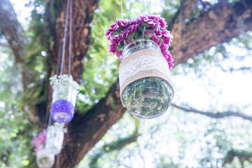 Various flowers in mason jars hanging from trees over wedding ceremony