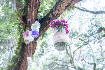 Various flowers in mason jars hanging from trees over wedding ceremony
