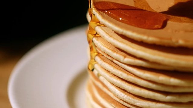 Close up maple syrup pouring on the pancakes. Black background. Traditional american food for breakfast  
