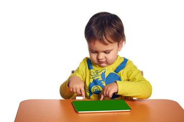 Young child girl is using tablet while sitting at table, isolated over white background
