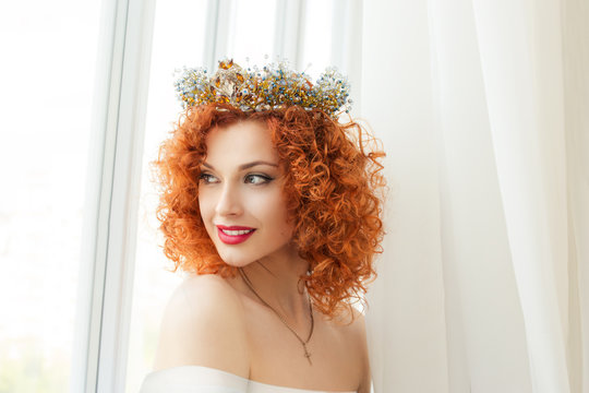 Beautiful red head  bride curly woman with crown fashion model person girl looking through window to the side thinking about future boyfriend groom new family isolated indoor white curtains background